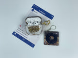 Clear earbud case filled with golden brown liquid glitter, attached to a gold cat-shaped clip and a miniature vinyl record keychain.