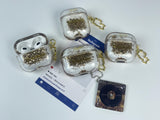 Clear earbud case filled with golden brown liquid glitter, attached to a gold cat-shaped clip and a miniature vinyl record keychain.