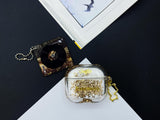 Clear earbud case filled with golden brown liquid glitter, attached to a gold cat-shaped clip and a miniature vinyl record keychain.