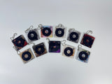 A collection of 11 square acrylic keychains featuring spinning miniature vinyl records and different aesthetic album artwork on a white background.