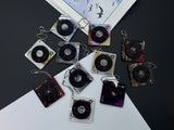 A collection of 11 square acrylic keychains featuring spinning miniature vinyl records and different aesthetic album artwork on a white background.