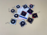 A collection of 11 square acrylic keychains featuring spinning miniature vinyl records and different aesthetic album artwork on a white background.