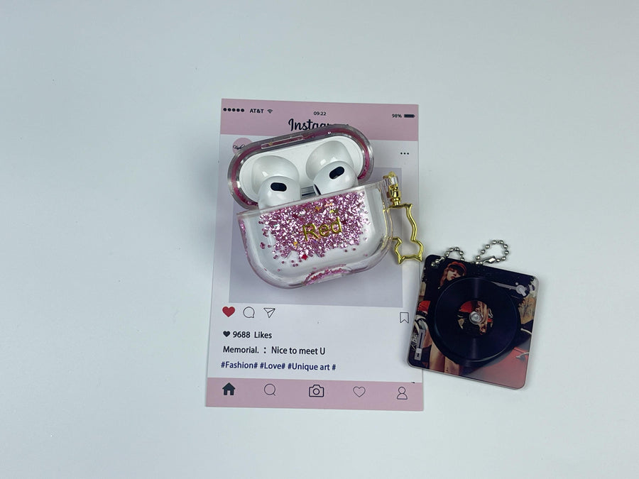 Clear earbud case filled with red and pink liquid glitter, attached to a gold cat-shaped clip and a miniature vinyl record keychain.