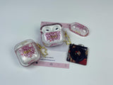 Clear earbud case filled with red and pink liquid glitter, attached to a gold cat-shaped clip and a miniature vinyl record keychain.