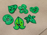 Six interchangeable green silicone leaf masks for a customizable earbud case, featuring heart, star, butterfly, and whisker shapes.