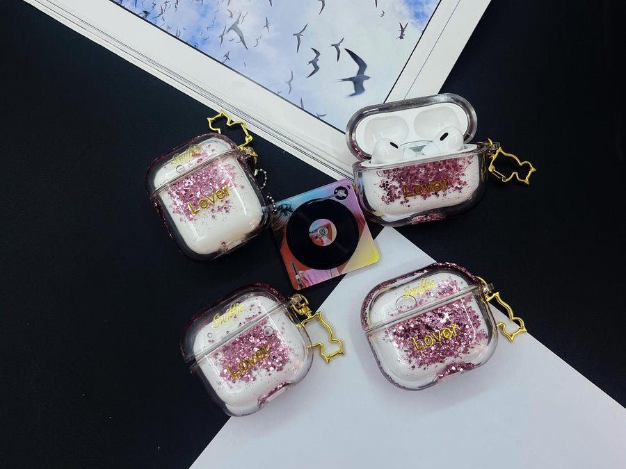 Clear earbud case filled with pink liquid glitter, attached to a gold cat-shaped clip and a miniature vinyl record keychain.