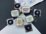 Clear earbud case filled with pink liquid glitter, attached to a gold cat-shaped clip and a miniature vinyl record keychain.