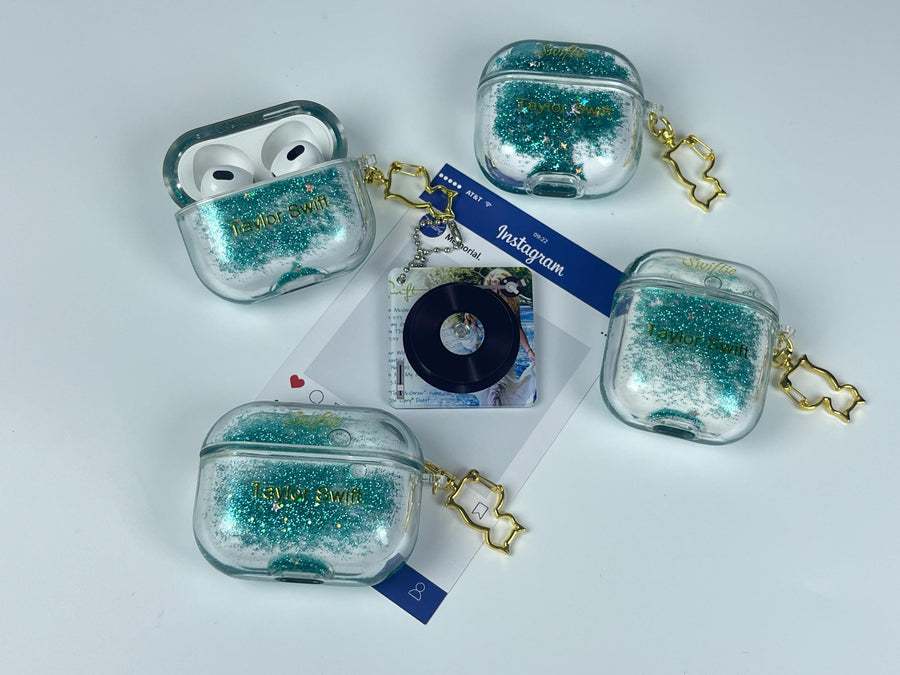 Clear earbud case filled with emerald green liquid glitter, attached to a gold cat-shaped clip and a miniature vinyl record keychain.