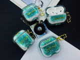 Clear earbud case filled with emerald green liquid glitter, attached to a gold cat-shaped clip and a miniature vinyl record keychain.