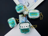 Clear earbud case filled with emerald green liquid glitter, attached to a gold cat-shaped clip and a miniature vinyl record keychain.