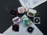 Clear earbud case filled with emerald green liquid glitter, attached to a gold cat-shaped clip and a miniature vinyl record keychain.