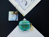 Clear earbud case filled with emerald green liquid glitter, attached to a gold cat-shaped clip and a miniature vinyl record keychain.