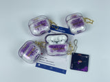 Clear earbud case filled with royal purple liquid glitter, attached to a gold cat-shaped clip and a miniature vinyl record keychain.