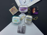 Clear earbud case filled with royal purple liquid glitter, attached to a gold cat-shaped clip and a miniature vinyl record keychain.