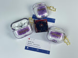 Clear earbud case filled with holographic lavender and blue liquid glitter, attached to a gold cat-shaped clip and a miniature vinyl record keychain.