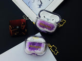 Clear earbud case filled with holographic lavender and blue liquid glitter, attached to a gold cat-shaped clip and a miniature vinyl record keychain.