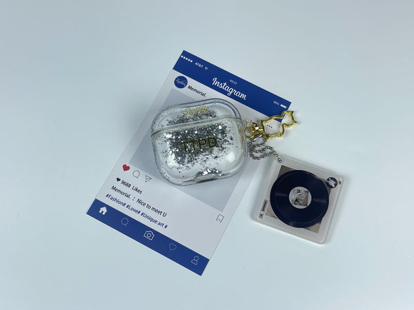 Clear earbud case filled with ghostly silver grayscale liquid glitter, attached to a gold cat-shaped clip and a miniature vinyl record keychain.