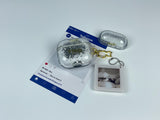 Clear earbud case filled with ghostly silver grayscale liquid glitter, attached to a gold cat-shaped clip and a miniature vinyl record keychain.