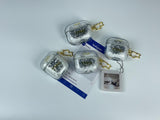 Clear earbud case filled with ghostly silver grayscale liquid glitter, attached to a gold cat-shaped clip and a miniature vinyl record keychain.
