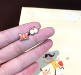 A pair of tiny resin stud earrings featuring a mismatched design of a happy corgi face and a corgi backside.