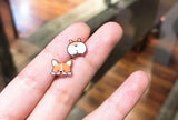 A pair of tiny resin stud earrings featuring a mismatched design of a happy corgi face and a corgi backside.