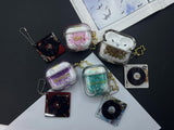 Clear earbud case filled with silver-grey liquid glitter, attached to a gold cat-shaped clip and a miniature vinyl record keychain.