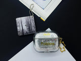 Clear earbud case filled with silver-grey liquid glitter, attached to a gold cat-shaped clip and a miniature vinyl record keychain.