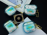 Clear, blue-tinted earbud case filled with iridescent blue liquid glitter, attached to a gold cat-shaped clip and a miniature vinyl record keychain.