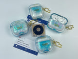 Clear, blue-tinted earbud case filled with iridescent blue liquid glitter, attached to a gold cat-shaped clip and a miniature vinyl record keychain.