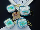 Clear, blue-tinted earbud case filled with iridescent blue liquid glitter, attached to a gold cat-shaped clip and a miniature vinyl record keychain.