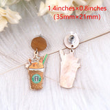 A pair of acrylic dangle earrings featuring a sleepy orange cat inside an iced coffee cup with whipped cream, hanging from marbled beige resin studs.