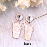 A pair of acrylic dangle earrings featuring a sleepy orange cat inside an iced coffee cup with whipped cream, hanging from marbled beige resin studs.